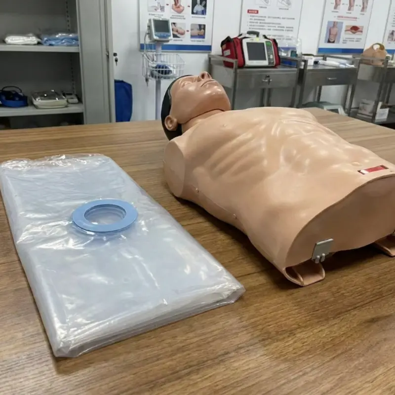 Rollo de bolsas pulmonares transparentes junto a un maniquí de reanimación cardiopulmonar sobre una mesa de madera.