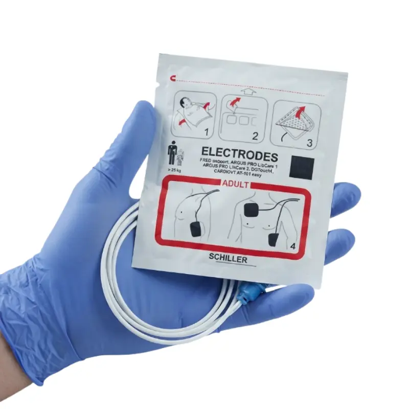 Mano con guante azul de nitrilo sosteniendo el envase y el cable con clavija de los Schiller Fred Easyport electrodos adulto.