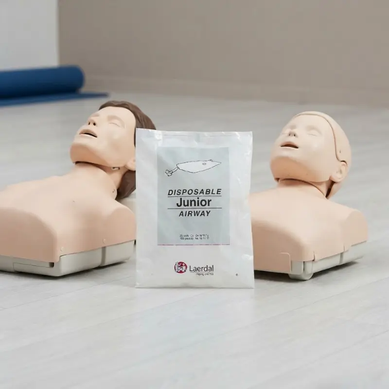 Paquete de vías respiratorias pediátricas Laerdal flanqueado por dos maniquíes de RCP sobre el suelo.