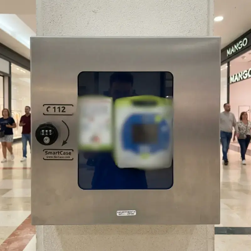 Vitrina gris SmartCase instalada en una columna de un centro comercial con transeúntes al fondo y escaparates de tiendas.