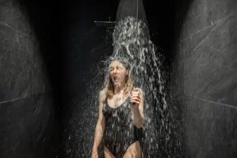 Mujer tomando una ducha de agua fría en un baño oscuro para activar la circulación y aliviar las piernas cansadas.