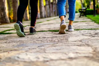 Personas caminando con calzado deportivo por un sendero de piedra en un parque para prevenir piernas cansadas.