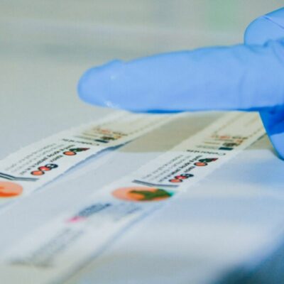 Primer plano de guante azul aplicando muestra sobre sensor reactivo de pulsera Celentis para detectar drogas en bebidas.