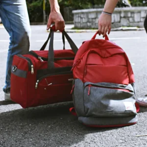 Dos personas sosteniendo por las asas una mochila médica roja y gris y un bolso de emergencias sanitario rojo sobre el asfalto.