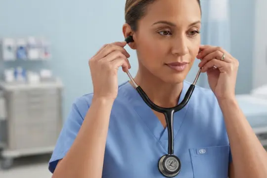 Personal sanitario ajustándose las olivas auriculares de un fonendoscopio Littmann negro en consulta.