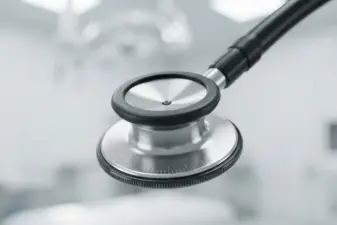 Primer plano macro de la campana metálica y el diafragma de un fonendoscopio frente a un fondo clínico difuminado.