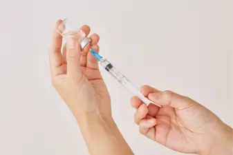 Manos sosteniendo un vial de vidrio transparente y una jeringa con aguja fina durante la preparación de microinyecciones.