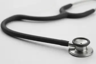 Primer plano del tubo flexible y la campana metálica de un estetoscopio Littmann negro sobre fondo claro.