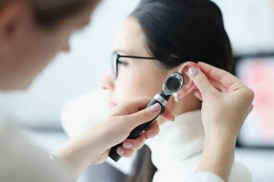 Médico examinando el canal auditivo de un paciente con un otoscopio en una consulta médica.