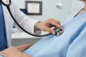 Profesional sanitario auscultando el tórax de un paciente con un fonendoscopio en una consulta médica.