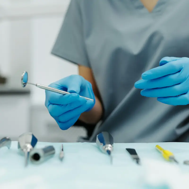 Instrumental dental metálico sobre una bandeja quirúrgica y manos con guantes azules examinando las herramientas.
