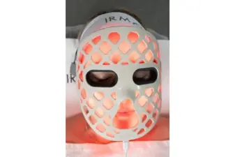 Paciente con los ojos cerrados usando la máscara facial Lumina Face con luz roja en una camilla de clínica estética.