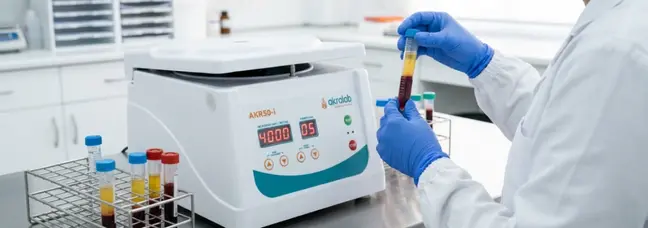Personal sanitario con guantes azules manipulando un tubo con plasma separado frente a la centrifugadora AKR50-i en laboratorio.