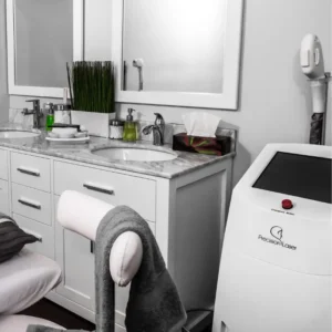 Aparato de láser de diodo Precision Laser blanco con botón de emergencia rojo junto a lavabos de mármol en clínica estética.